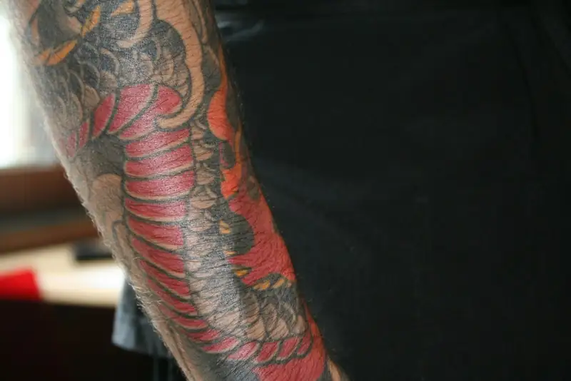 Braço com tatuagem colorida de dragão, em vermelho e laranja, no estilo oriental