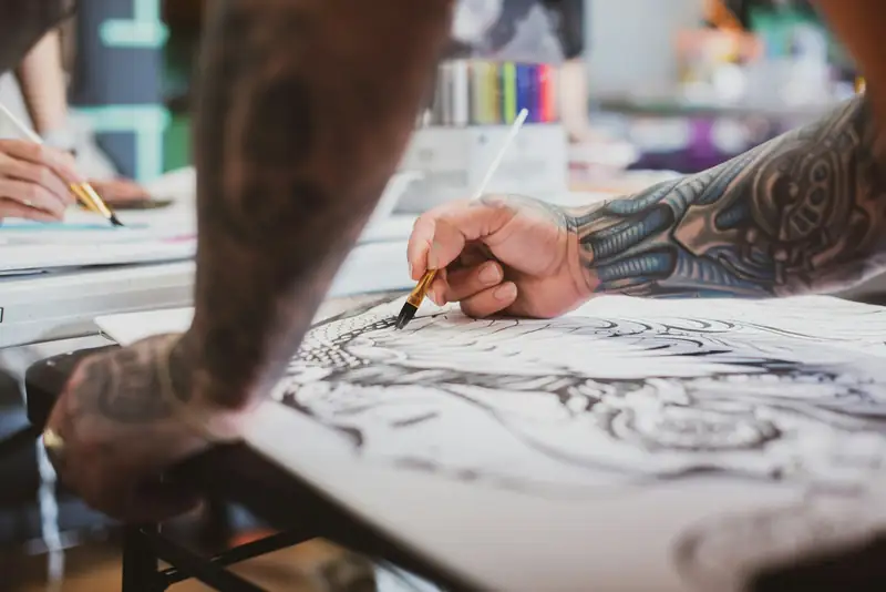 Braço tatuado pintando com pincel um desenho em preto e branco no papel
