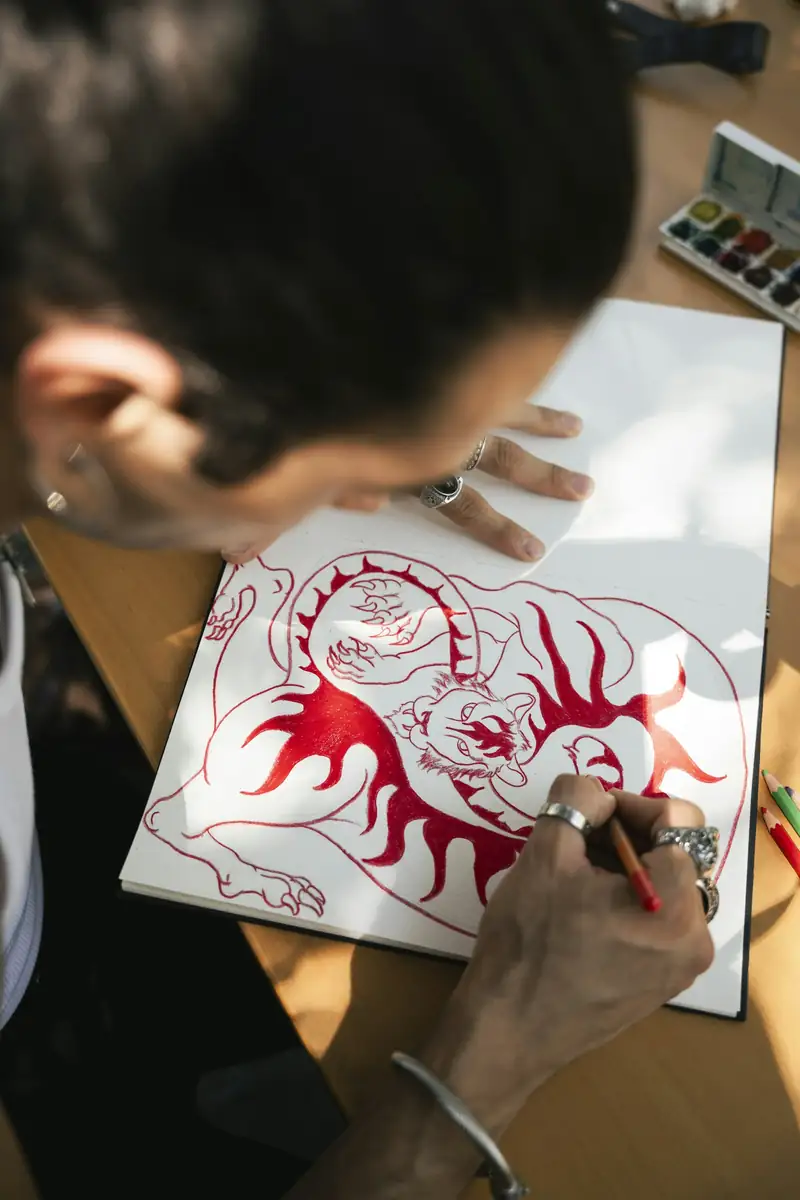 Artista desenhando em vermelho um tigre com chamas num caderno de esboços