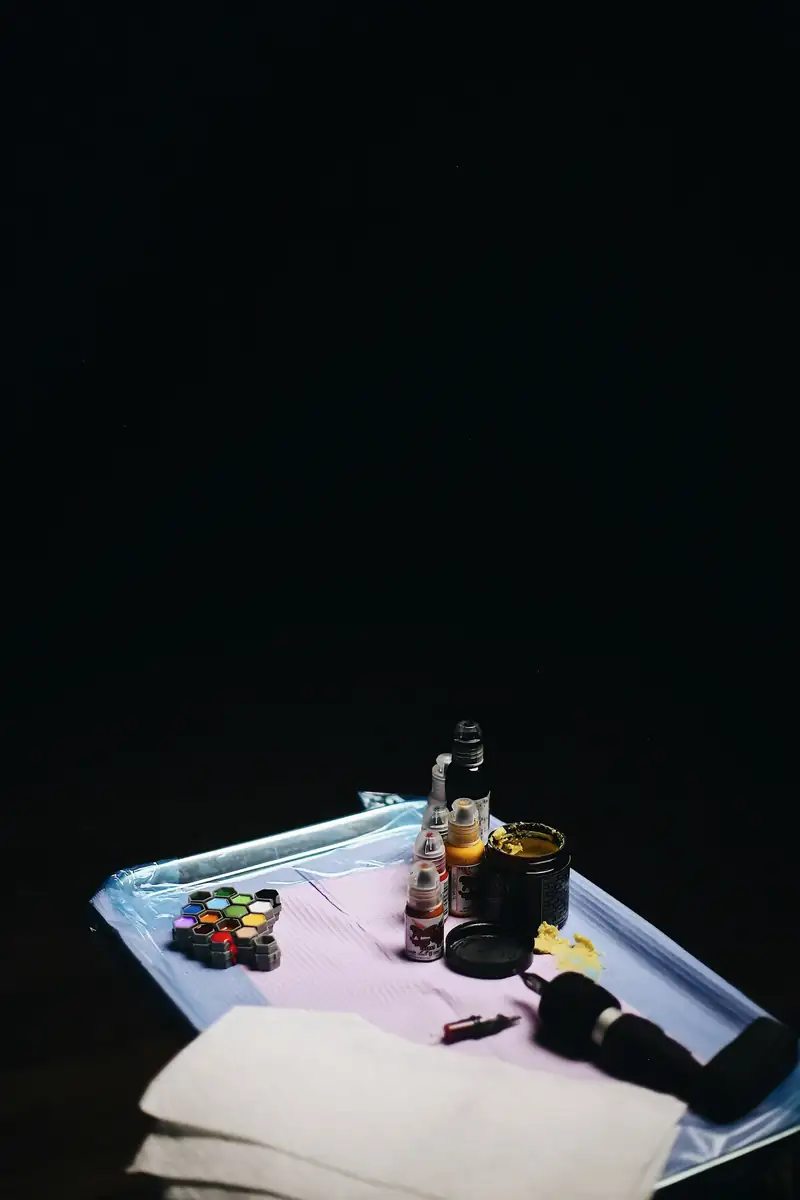 Bandeja com potes de tinta coloridos, frascos e a máquina, sobre fundo escuro