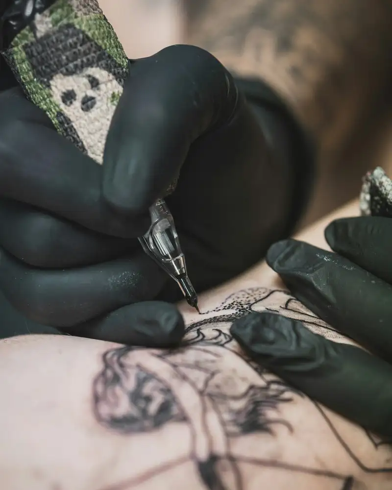 Close de mãos de luvas pretas fazendo o contorno de uma tatuagem na pele